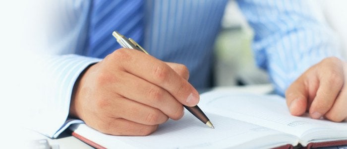 Stock image - A man uses a pen to write in a notebook